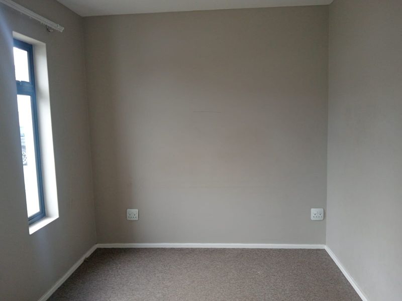 A clean, empty bedroom featuring neutral wall paint, carpeted flooring, and a single window, providing a blank canvas for personalization.