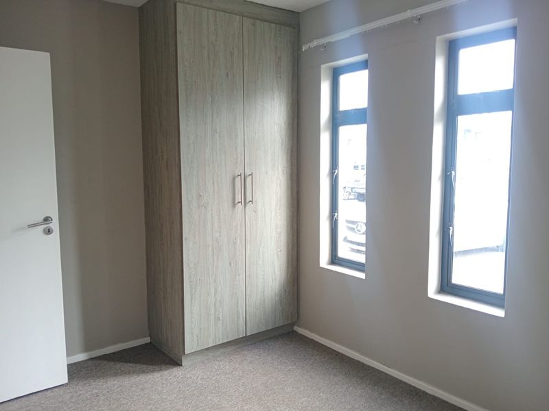 A clean, empty bedroom featuring neutral wall tones, carpeted flooring, and a modern built-in wardrobe with wood-grain finish.