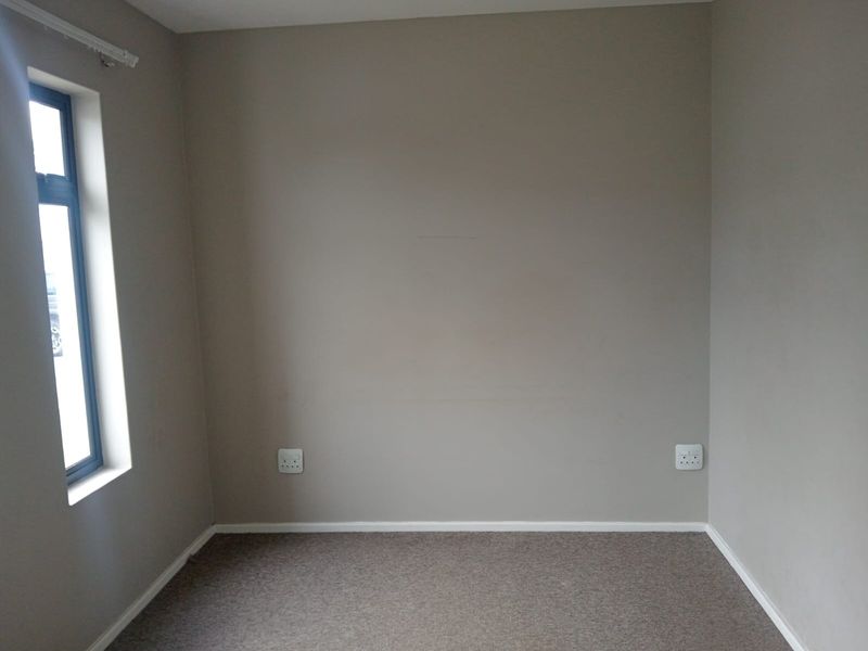 A clean, empty bedroom featuring neutral wall paint, carpeted flooring, and a single window, providing a versatile space ready for personalization.