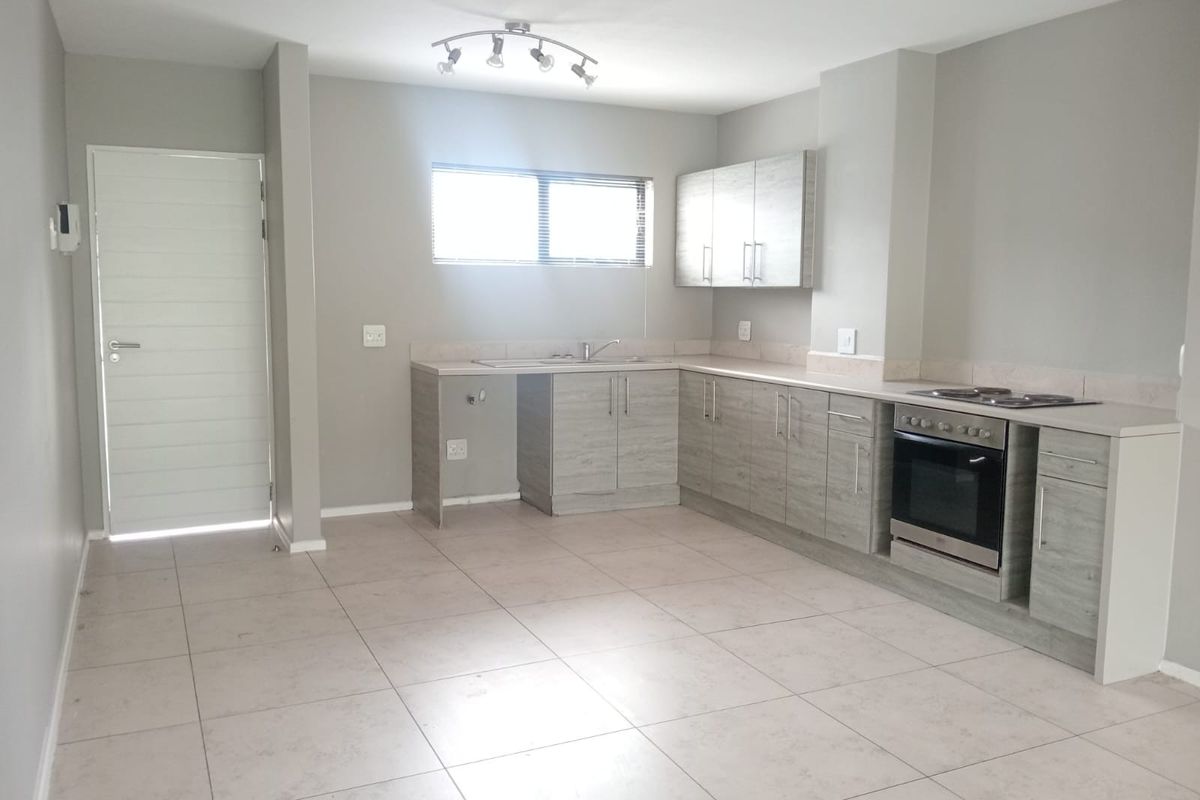 A clean, modern kitchen featuring light wood-grain cabinetry, integrated oven and hob, tiled flooring, and ample counter space in an open-plan layout.