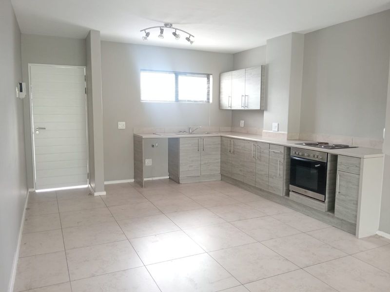 A clean, modern kitchen featuring light wood-grain cabinetry, integrated oven and hob, tiled flooring, and ample counter space in an open-plan layout.