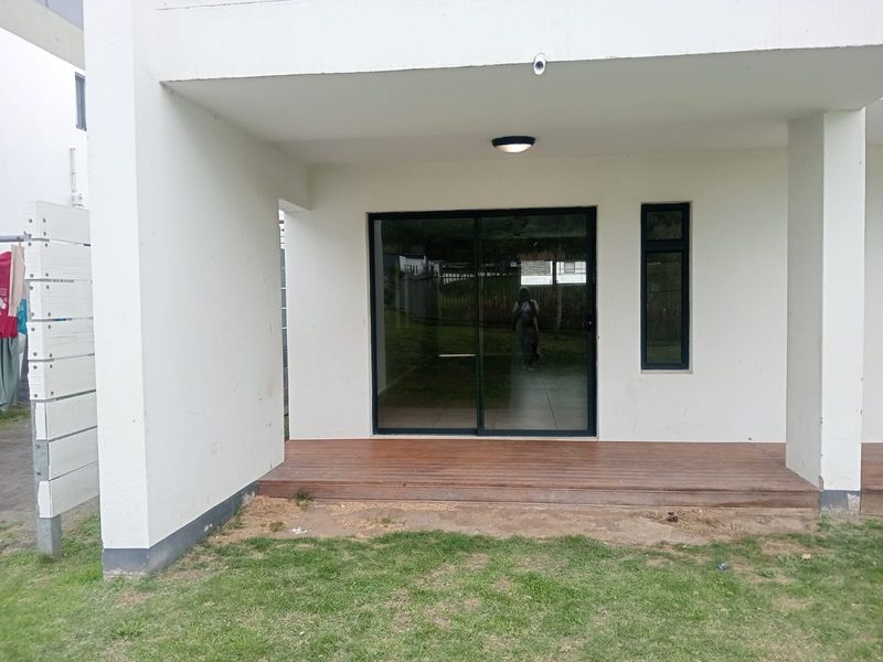 A covered patio area featuring timber decking, a sliding glass door, and a fixed window, providing direct access to the garden.