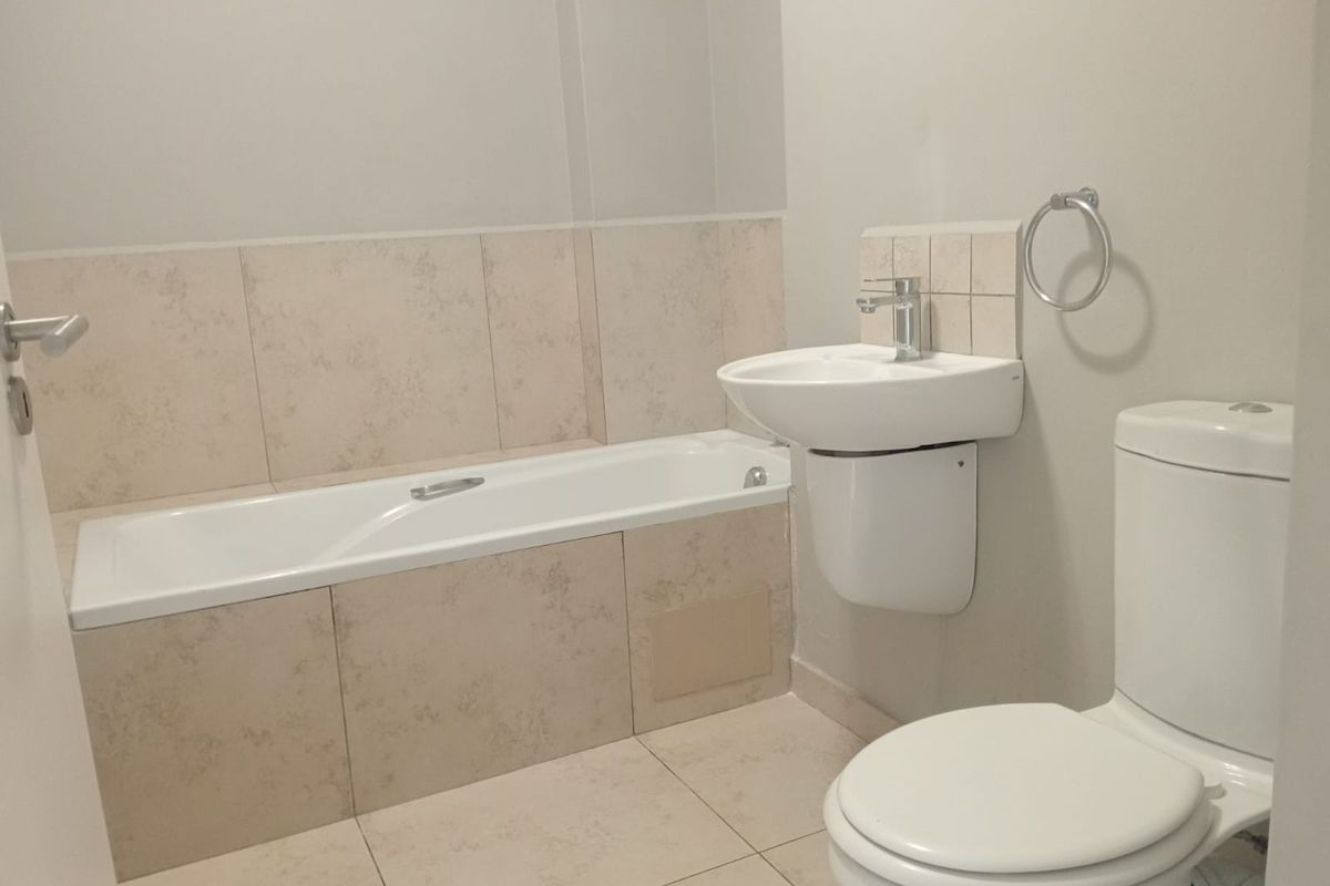 A clean, functional bathroom featuring a built-in bathtub, wall-mounted basin, and toilet with neutral tiled finishes.
