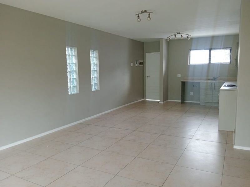 Spacious open-plan living and kitchen area featuring neutral tiled flooring, glass block windows, and functional built-in kitchen cabinetry.