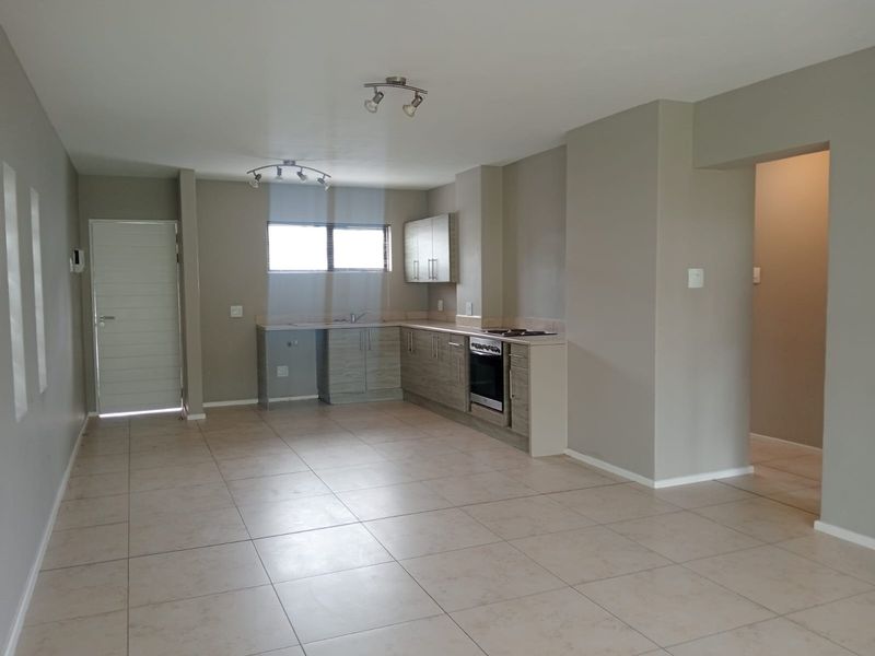 An open-plan living and kitchen area featuring neutral tiled flooring, modern cabinetry, and a built-in oven, offering a clean and versatile space.