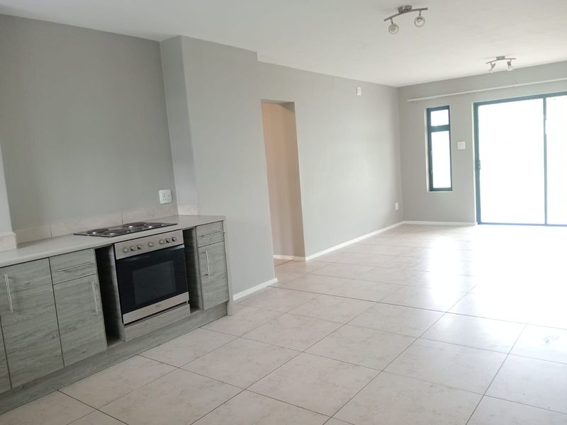 Spacious open-plan living area featuring tiled floors, a modern kitchen with built-in oven and hob, and sliding door access to the exterior.