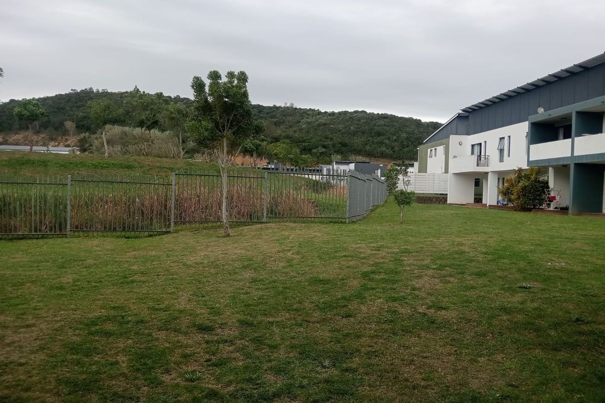 A view of the rear exterior of the apartment complex, featuring a large communal lawn area and metal perimeter fencing.