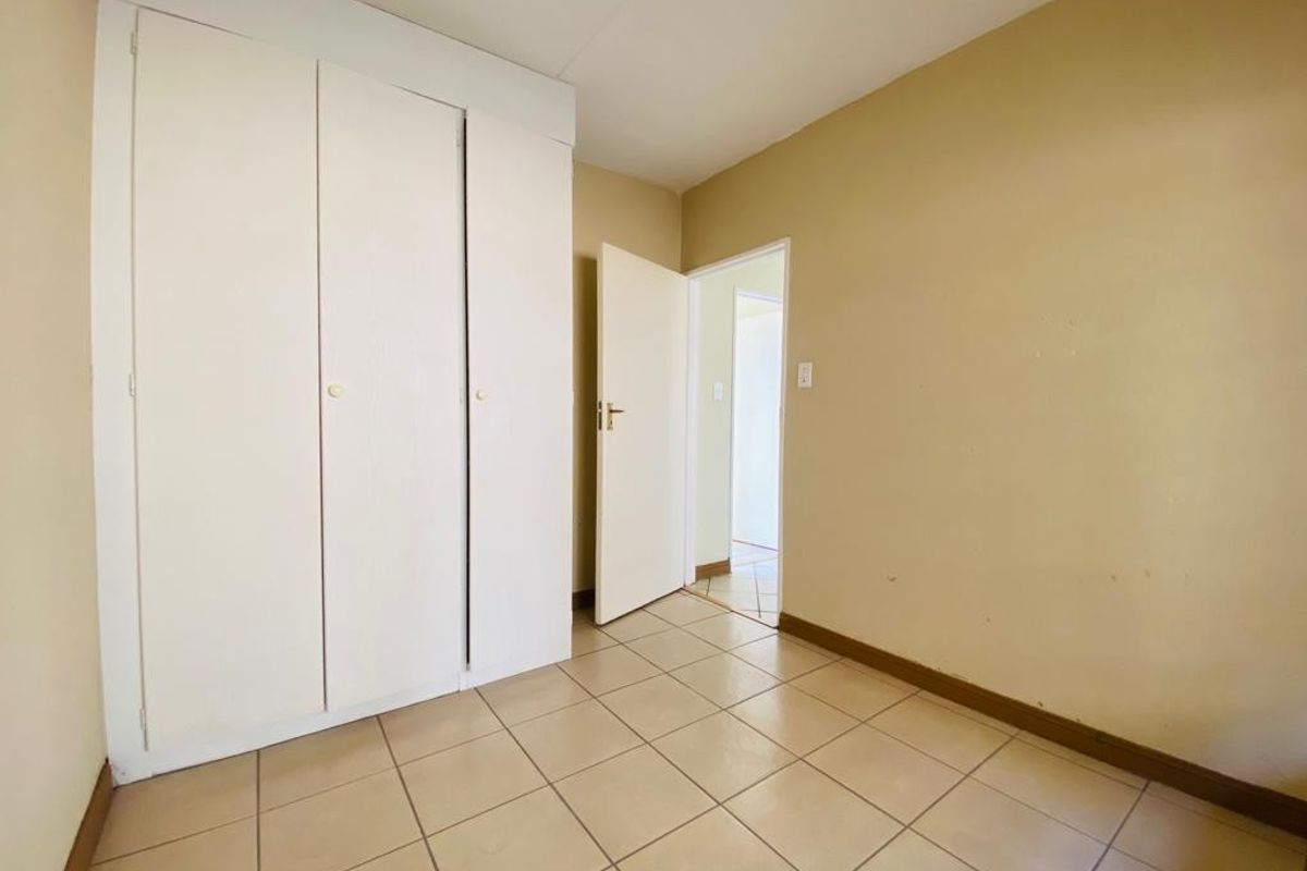 An empty bedroom featuring tiled flooring and built-in cupboards, requiring minor cosmetic updates to the wall finishes.