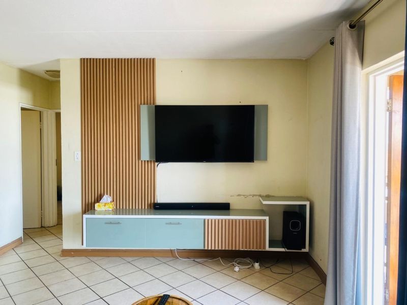 Living room featuring a timber slat feature wall, built-in floating media console, and ceramic floor tiles with access to an outdoor area.