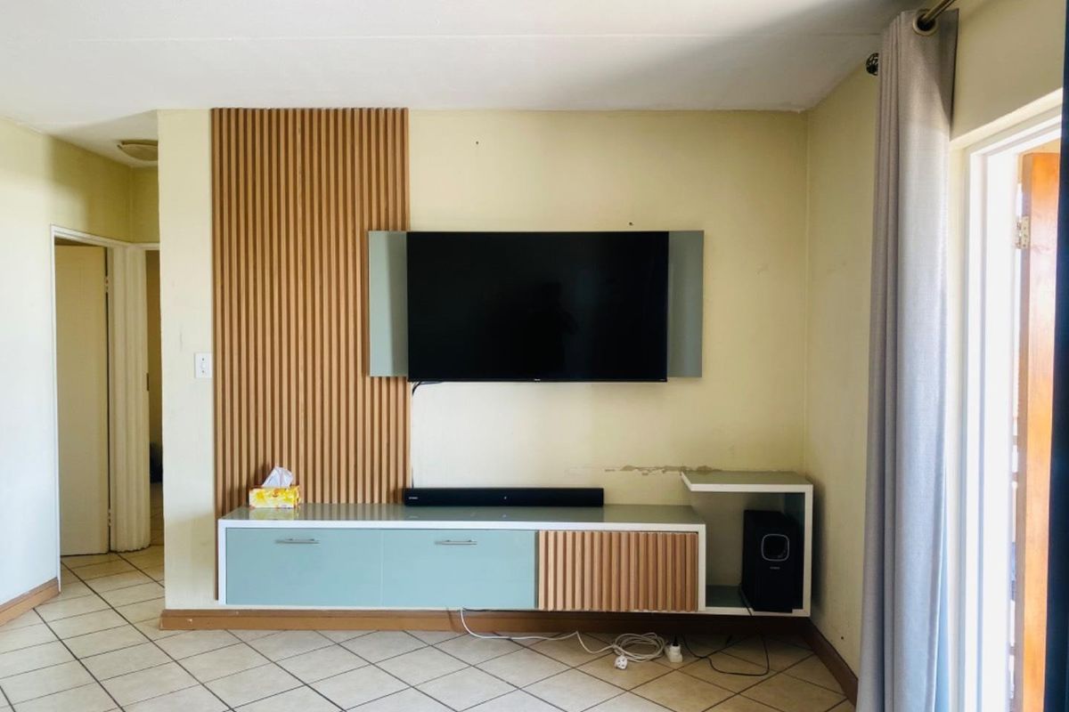 Living room featuring a timber slat feature wall, built-in floating media console, and ceramic floor tiles with access to an outdoor area.