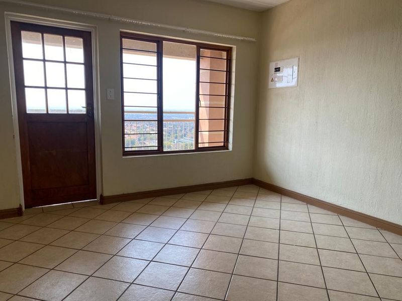 An empty living area featuring tiled flooring, a timber door, and security bars on the windows with views of the surrounding area.