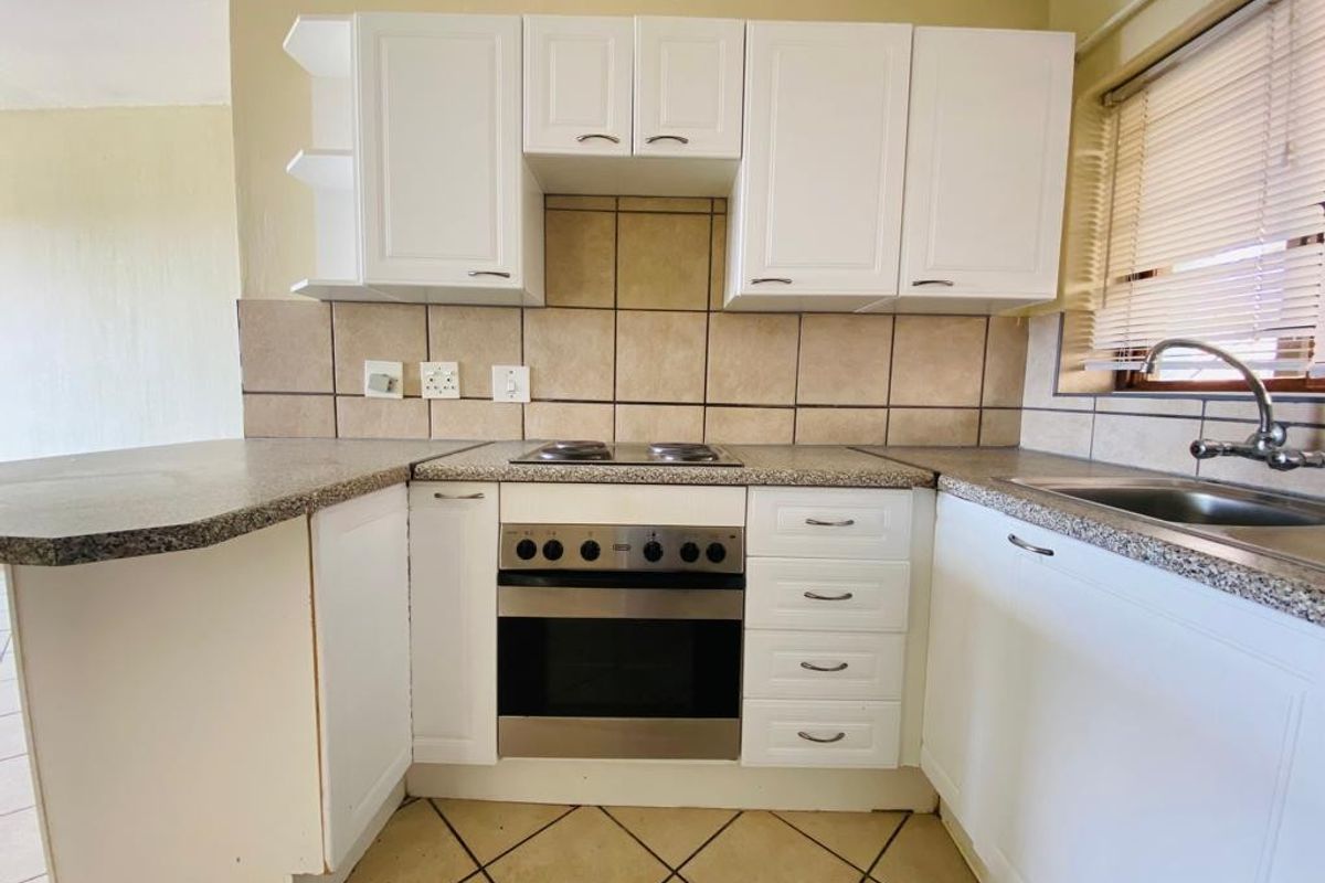 A functional kitchen featuring white cabinetry, laminate countertops, a built-in oven with electric hob, and a tiled backsplash.