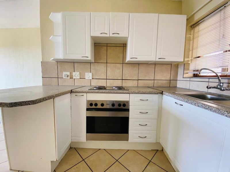 A functional kitchen featuring white cabinetry, laminate countertops, a built-in oven with electric hob, and a tiled backsplash.