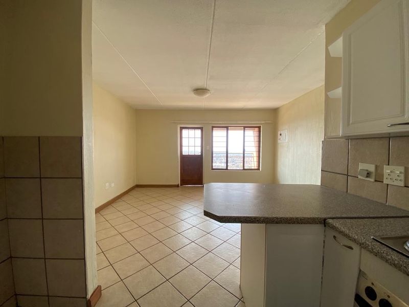 Open-plan living and kitchen area featuring tiled flooring, built-in cabinetry, and direct access to an exterior door with security gate.