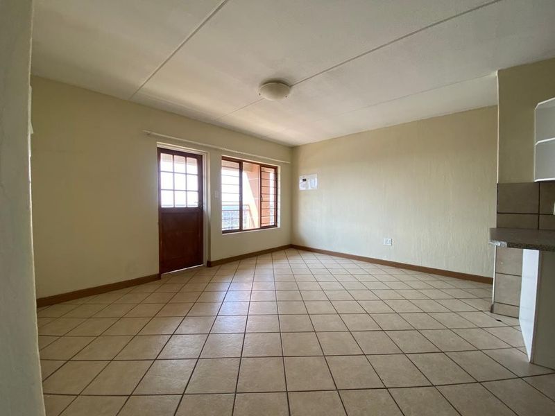 An empty open-plan living and kitchen area featuring tiled flooring, a security door, and neutral wall finishes, ready for personalization.