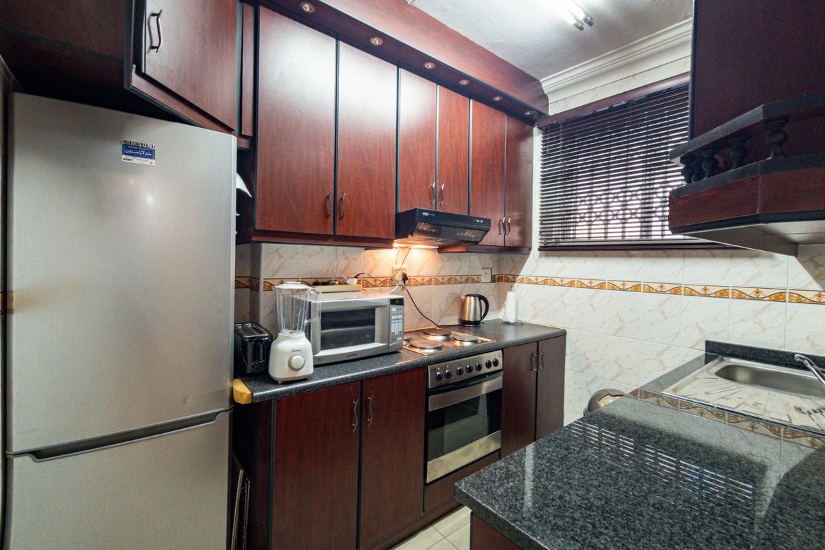 A functional kitchen featuring dark wood cabinetry, granite countertops, a built-in oven with hob, and a tiled backsplash.