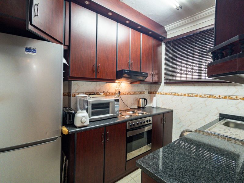 A functional kitchen featuring dark wood cabinetry, granite countertops, a built-in oven with hob, and a tiled backsplash.