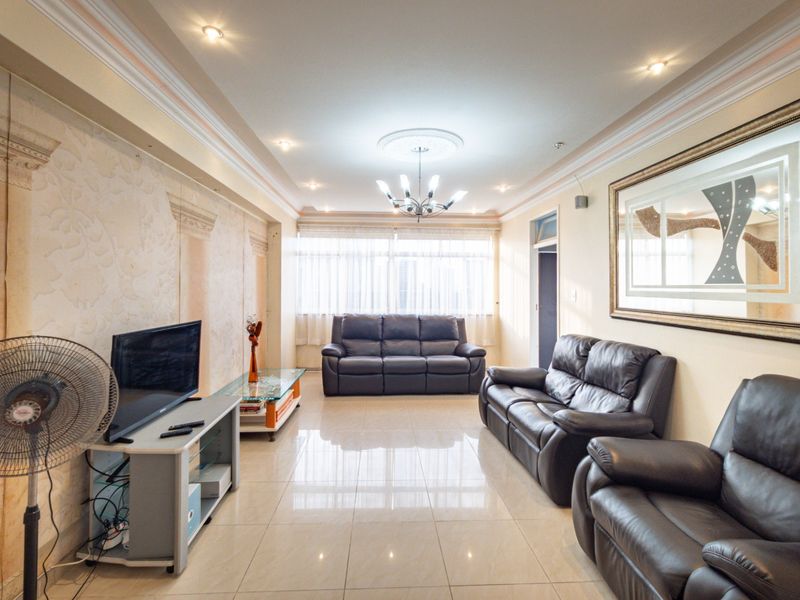 Spacious living room featuring tiled flooring, decorative ceiling molding, and a feature wall with classic architectural detailing.