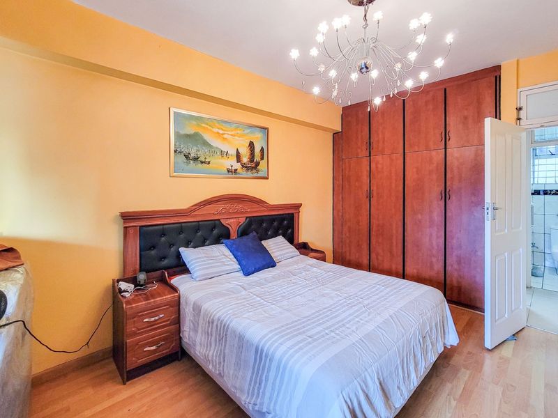 A bedroom featuring laminate flooring, a large built-in wooden wardrobe, and an en-suite bathroom, illuminated by a decorative chandelier.