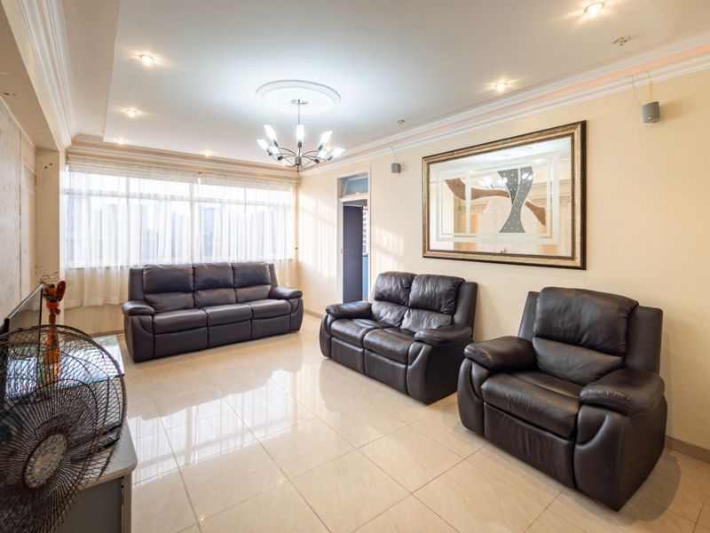 A spacious living room featuring polished tiled flooring, recessed ceiling lighting, and a decorative ceiling rose, offering a bright and neutral living space.