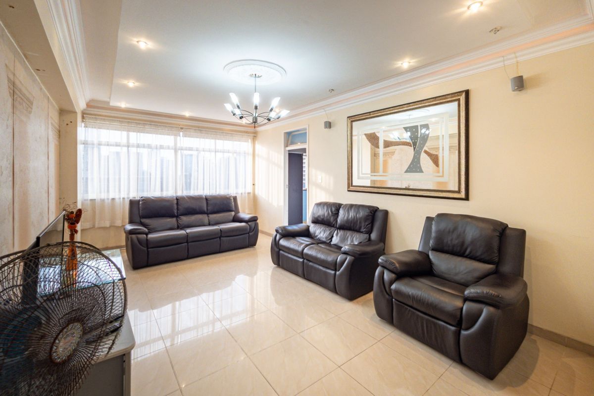 A spacious living room featuring polished tiled flooring, recessed ceiling lighting, and a decorative ceiling rose, offering a bright and neutral living space.