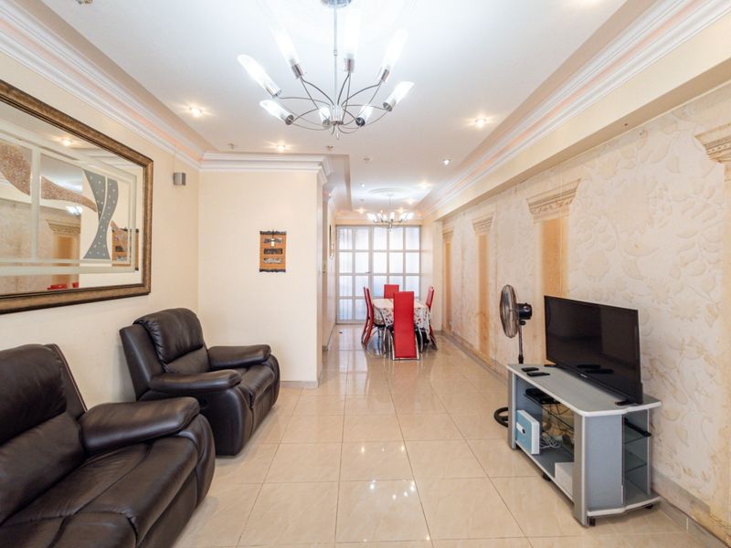 Open-plan living and dining area featuring tiled flooring, decorative wall molding, and recessed ceiling lighting with a glass-partitioned rear wall.