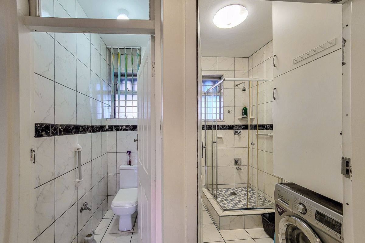 A functional bathroom featuring a separate toilet area and a shower enclosure with tiled finishes and built-in storage cabinetry.