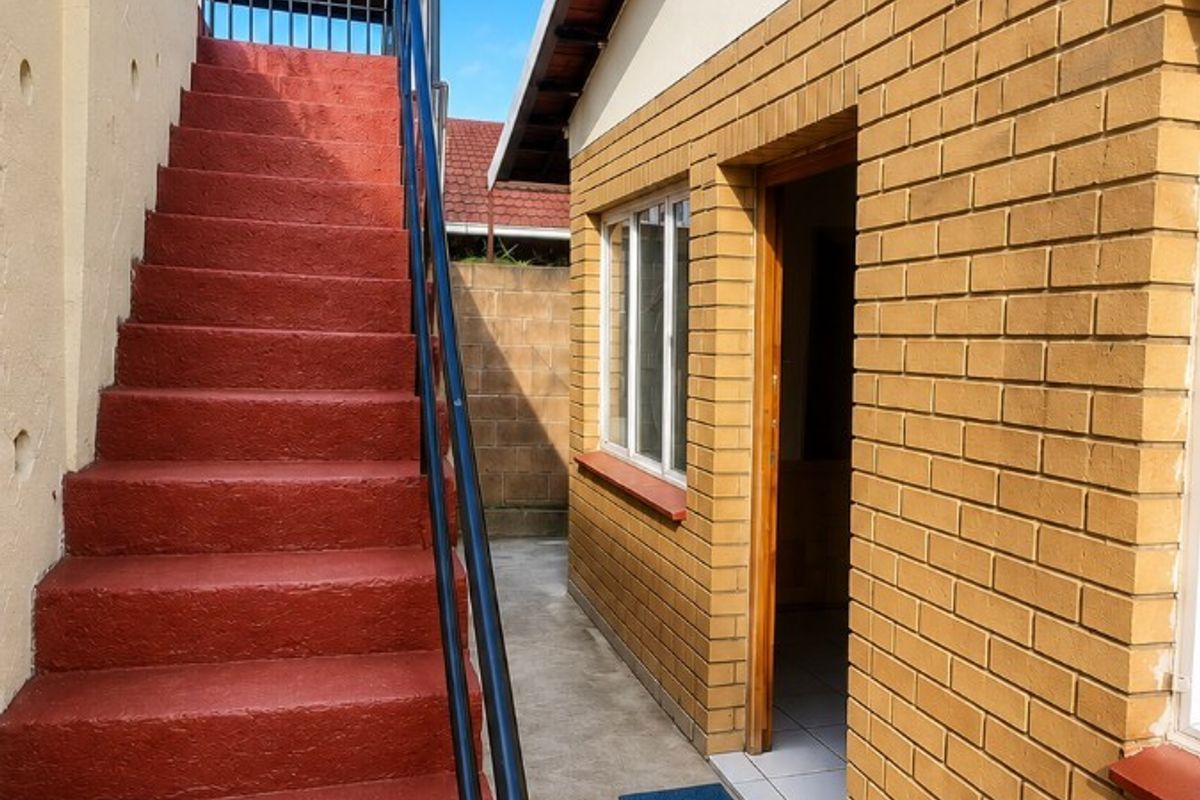 Rear exterior view featuring a painted concrete staircase with metal handrails leading to an upper level, alongside a face brick building facade.