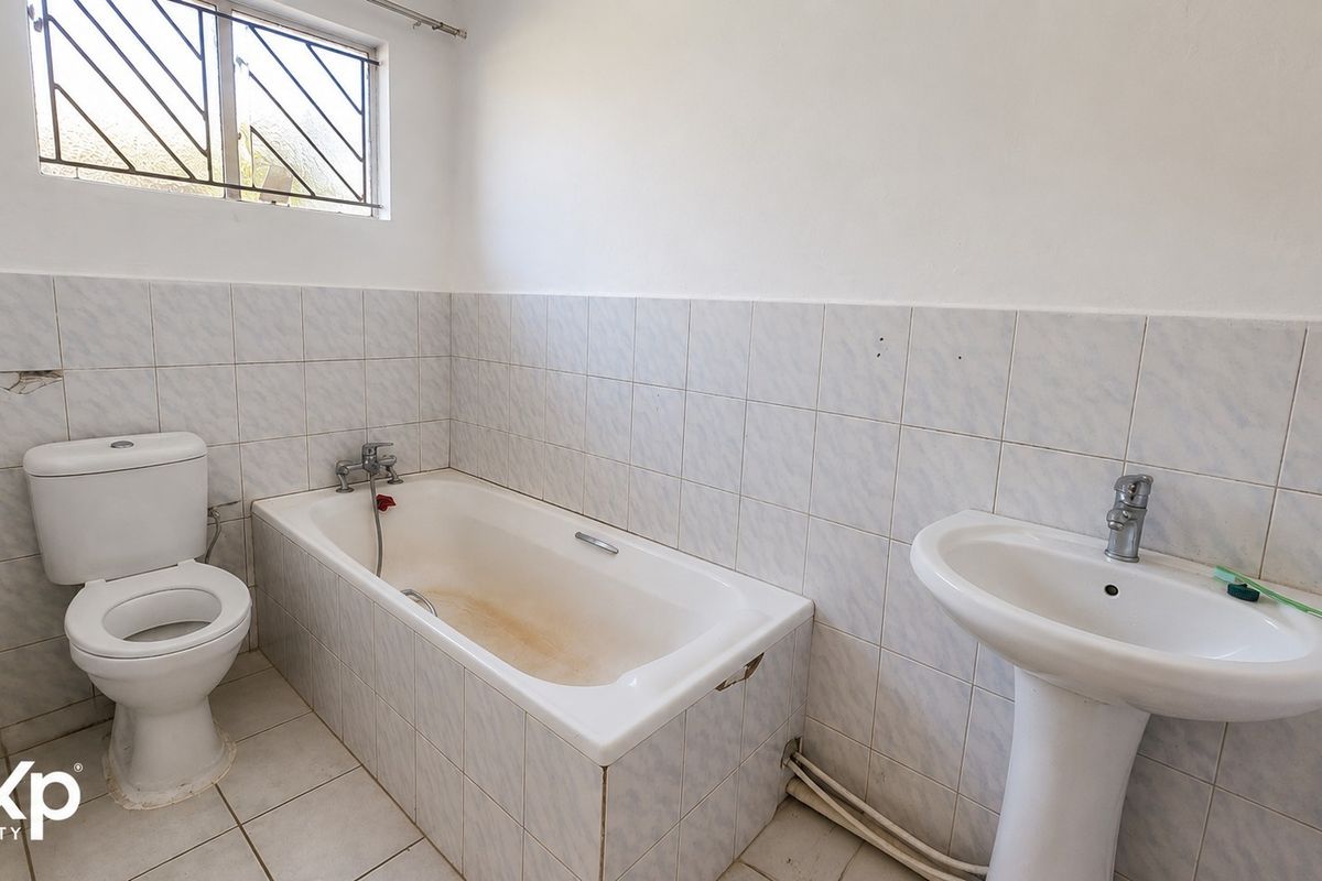 A functional bathroom featuring a pedestal basin, bathtub, and toilet, with tiled finishes throughout. The space is ready for cosmetic updates.