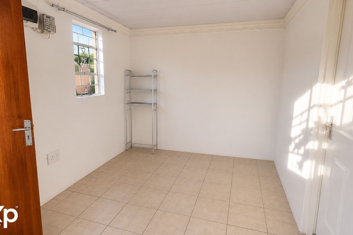 A clean, empty bedroom featuring neutral tiled flooring, a security-barred window, and an alarm system keypad.