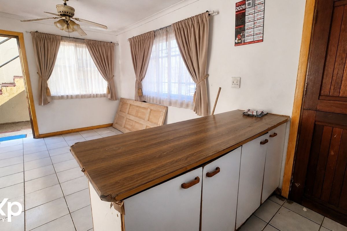 A dated kitchen area featuring tiled flooring, base cabinetry with laminate countertops, and a ceiling fan, requiring cosmetic updates to modernize the space.