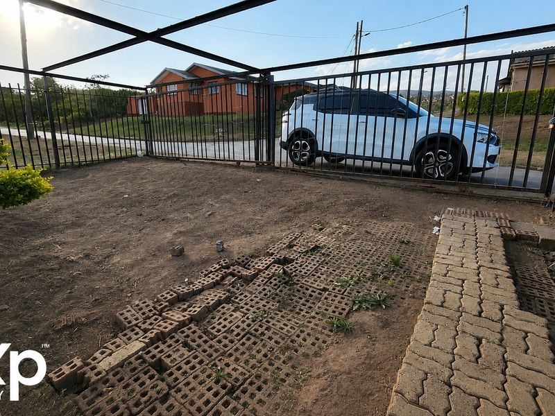 Front exterior view showing a gated driveway area with partial paving and unpaved ground.