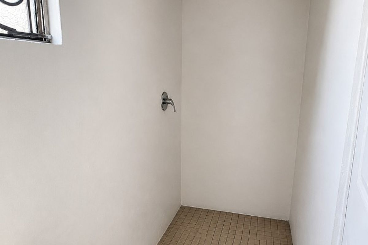 A compact bathroom shower area featuring tiled flooring, a wall-mounted shower mixer, and a window with security bars.