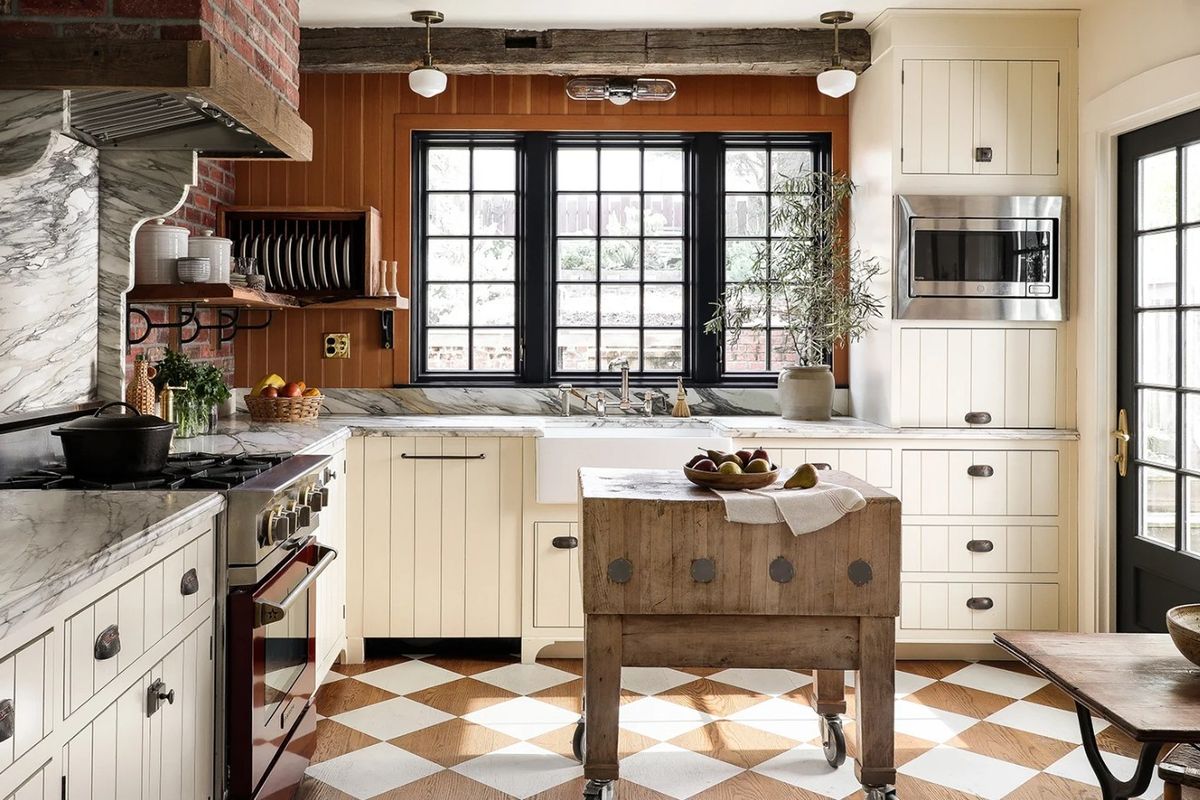 A beautifully appointed kitchen featuring marble countertops, a farmhouse sink, custom cabinetry, and a striking brick chimney breast with a gas range.