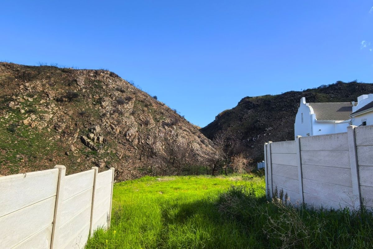 A vacant residential plot featuring a natural rocky hillside backdrop and precast concrete boundary walls on either side.