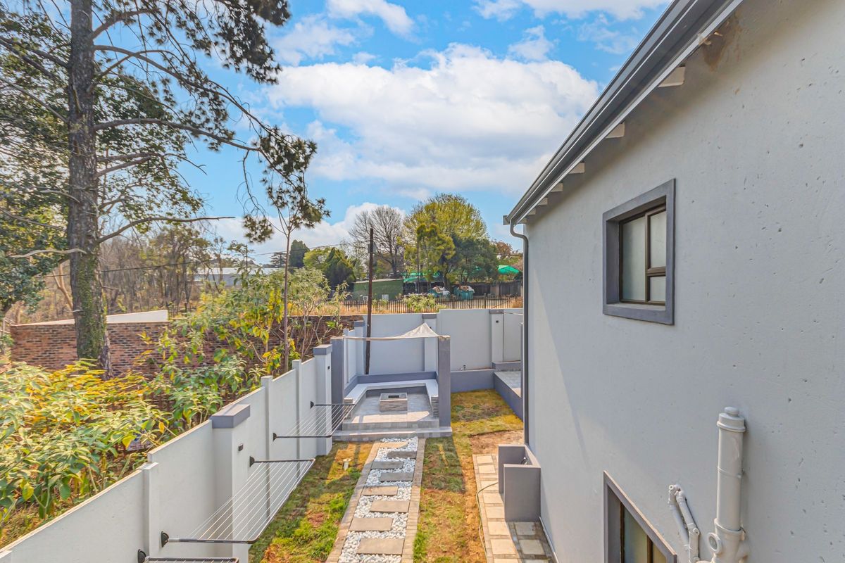 Rear exterior view featuring a landscaped garden, paved walkway, built-in fire pit area, and perimeter walling.