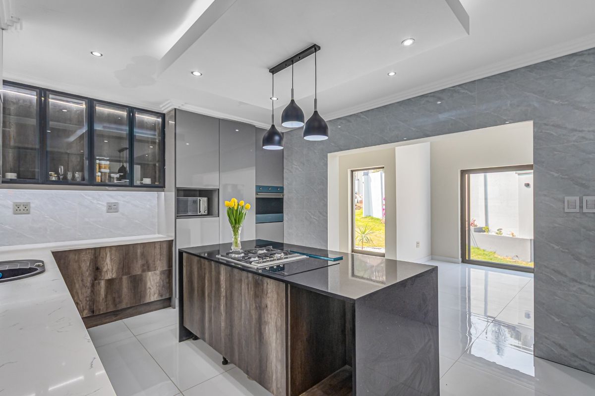Modern kitchen featuring a central island with gas hob, high-end cabinetry, stone countertops, and integrated appliances, opening to a bright outdoor area.