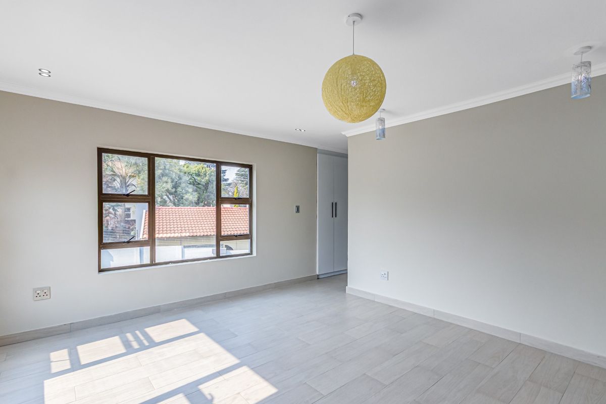 A bright and spacious bedroom featuring neutral wall tones, tiled flooring, built-in cupboards, and large aluminium-framed windows allowing for ample natural light.