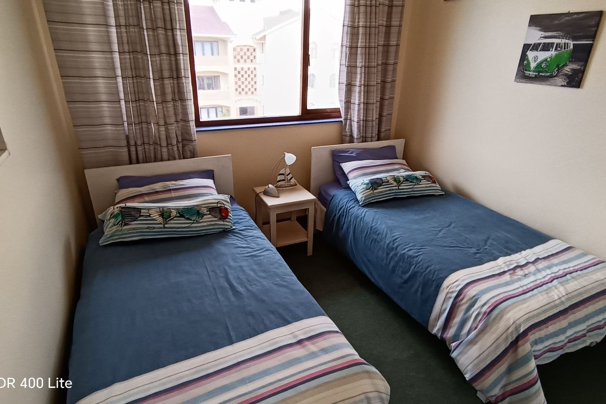 A compact bedroom featuring a window with curtains, carpeted flooring, and space for two single beds.