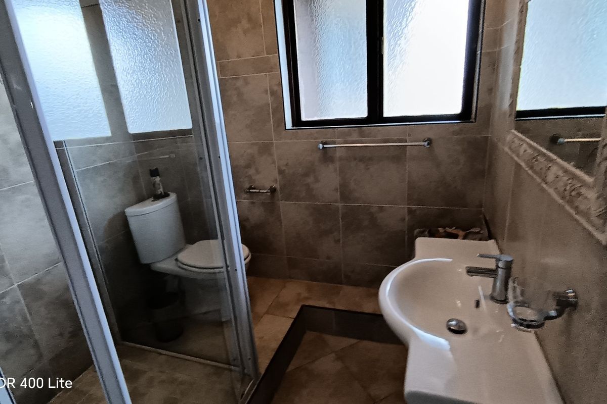 A functional bathroom featuring a shower enclosure, pedestal basin, and tiled finishes throughout, providing a clean and practical space.