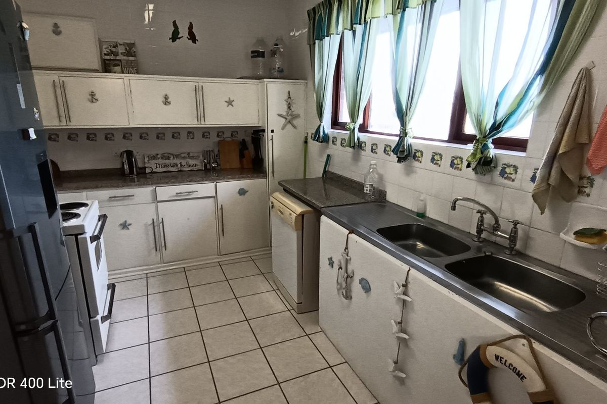 A functional kitchen featuring white cabinetry, granite countertops, a double stainless steel sink, and tiled flooring, offering a classic layout with ample storage space.