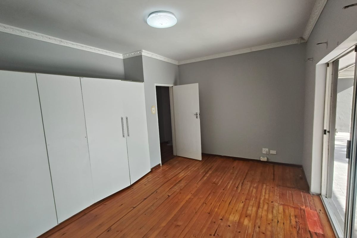 A spacious bedroom featuring polished hardwood flooring, built-in white cupboards, decorative ceiling cornices, and direct access to an outdoor area via sliding glass doors.