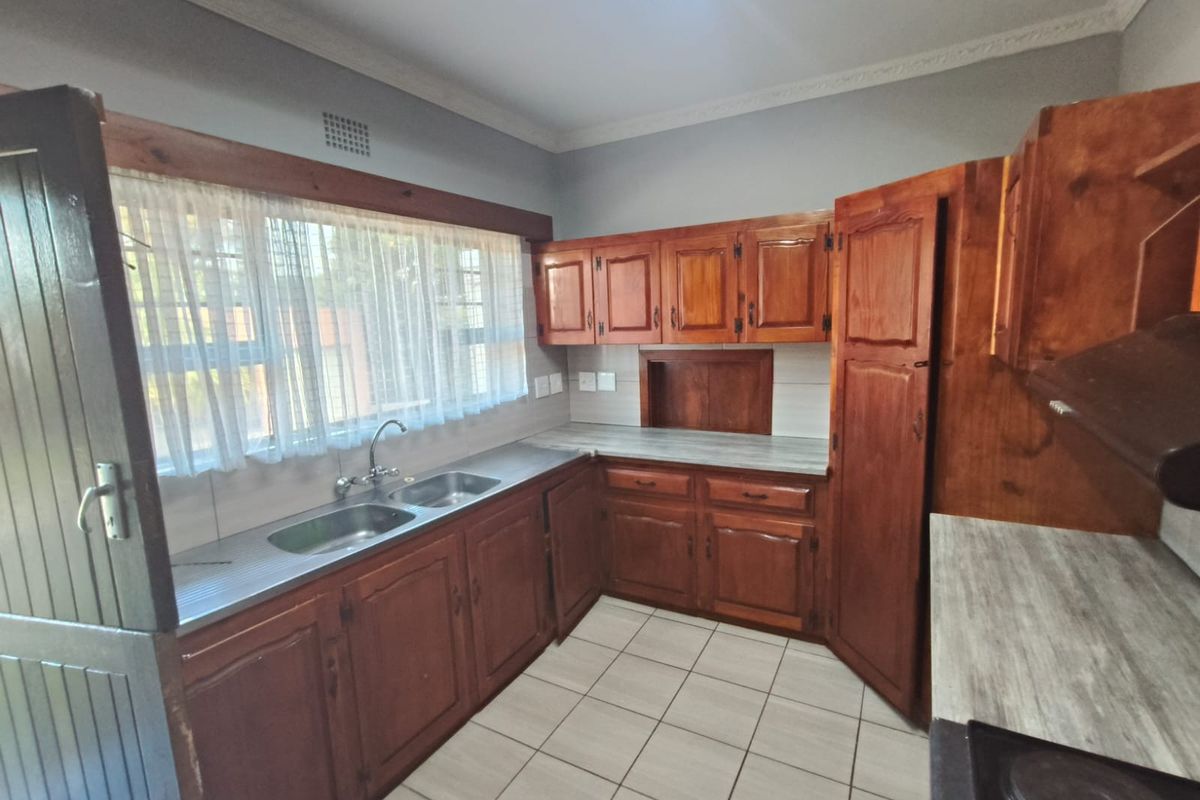 A functional kitchen featuring traditional wooden cabinetry, double stainless steel sink, and tiled flooring, offering a classic layout ready for modern updates.