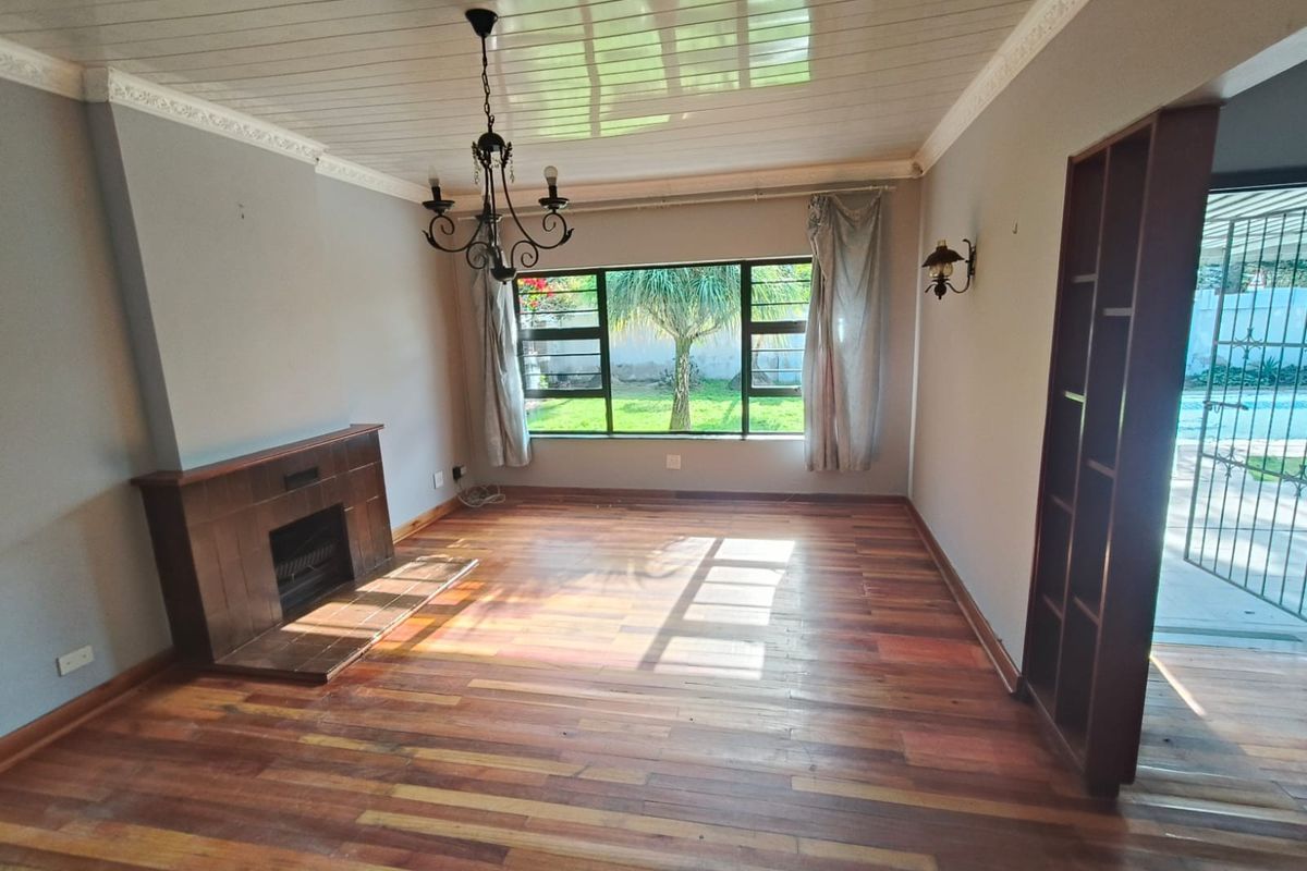 Spacious living room featuring hardwood flooring, a built-in fireplace, crown molding, and large windows overlooking the garden.