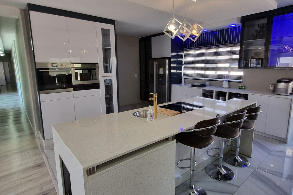 Modern kitchen featuring a large quartz-topped island, high-gloss cabinetry, integrated appliances, and stylish pendant lighting, seamlessly connected to a bright hallway.