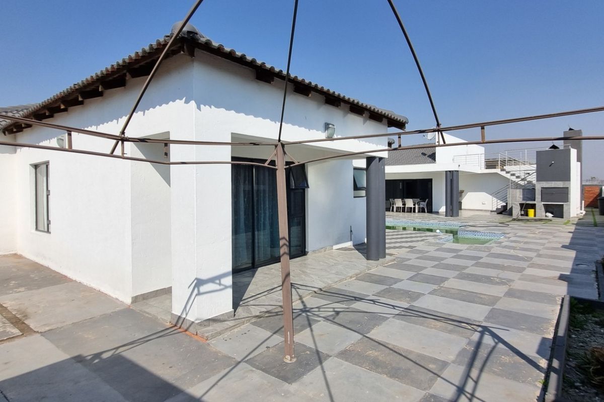 Rear exterior view featuring a tiled patio area, swimming pool, and built-in braai, providing a functional space for outdoor entertainment.