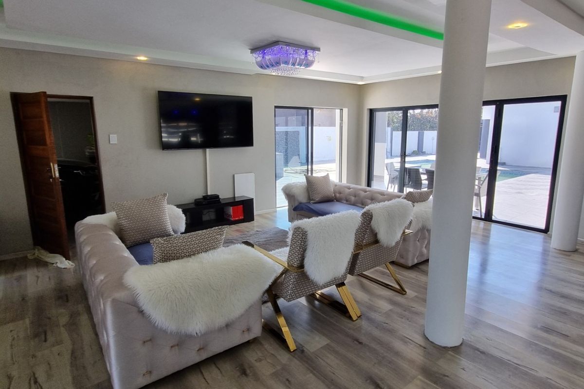 Spacious living area featuring modern laminate flooring, recessed ceiling lighting with cove accents, and large sliding glass doors providing access to the outdoor pool area.