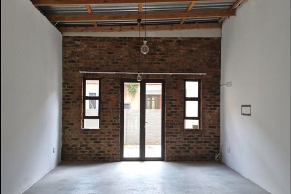 An open-plan living area featuring an exposed brick wall, polished concrete flooring, and high ceilings with exposed timber trusses and pendant lighting.