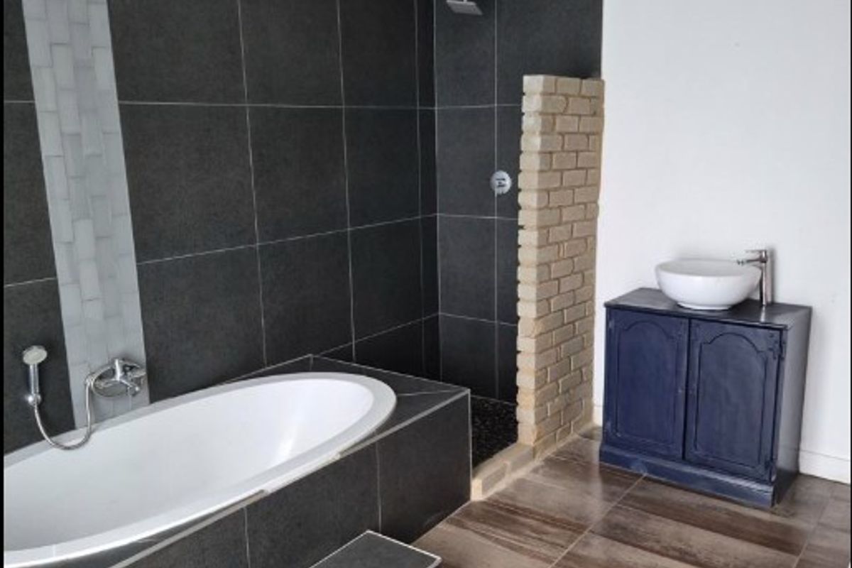 Modern bathroom featuring a built-in bathtub, walk-in shower with dark tiling, and a vanity unit with a vessel sink.