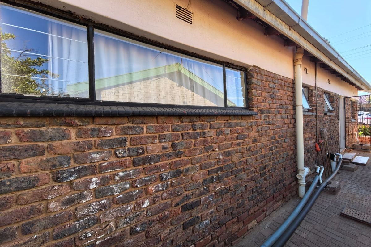 Rear exterior view of the property featuring face brick walls, aluminium window frames, and a paved walkway with visible drainage piping.